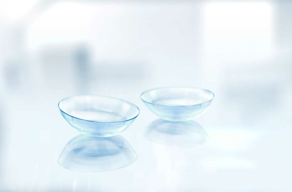 A close up of two contact lenses sitting on a white, reflective surface.