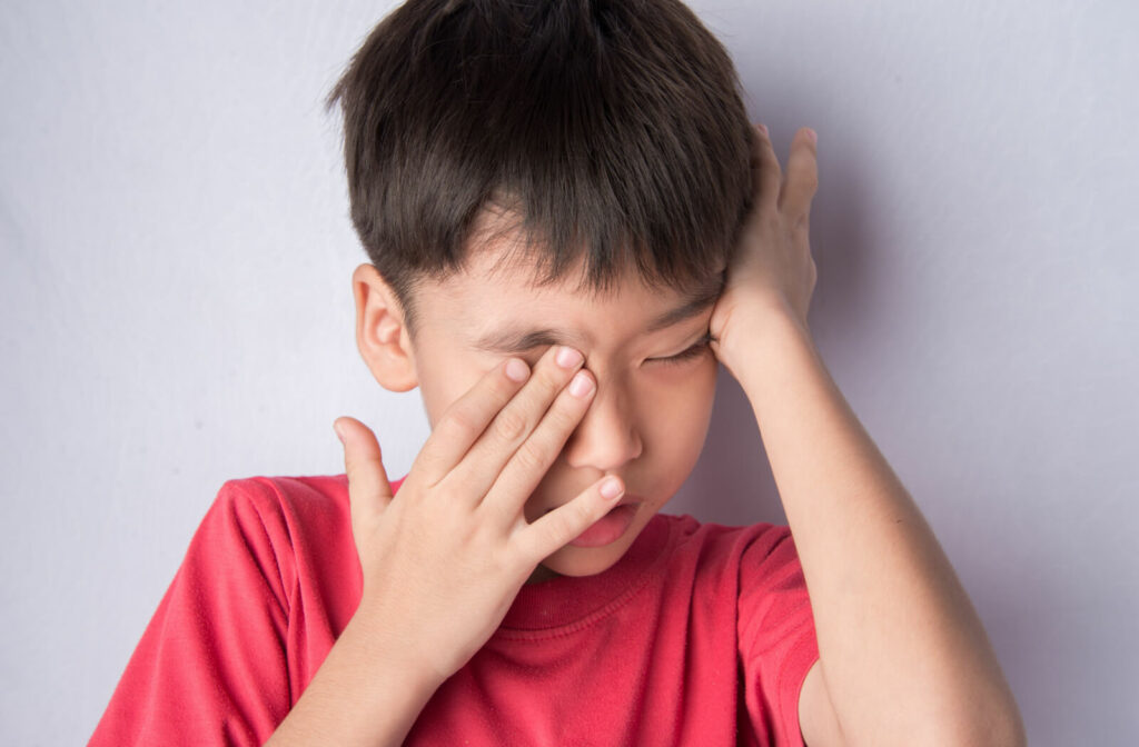 A little boy in a red shirt is rubbing his eyes with both hands. By rubbing your itchy eyes it’s possible to injure or cause other eye problem.