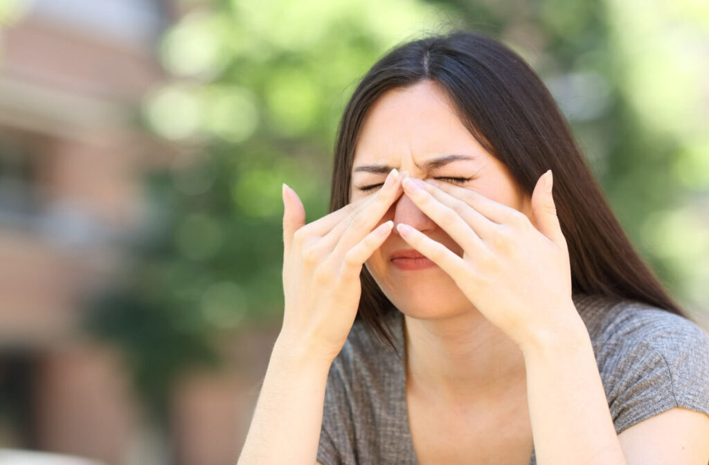 A woman is scratching her itchy dry eyes outdoors.
