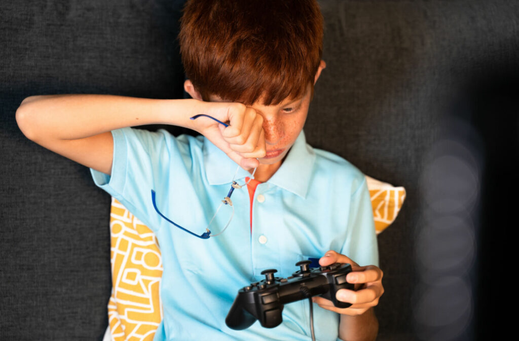 A boy playing video games is rubbing his eyes because of eye irritation due to prolong time on the screen.