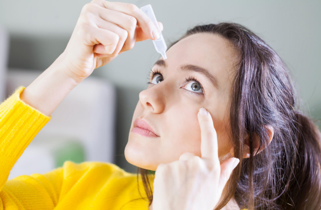 A woman holding a small bottle of eye drops in her right hand and putting them on left eye.