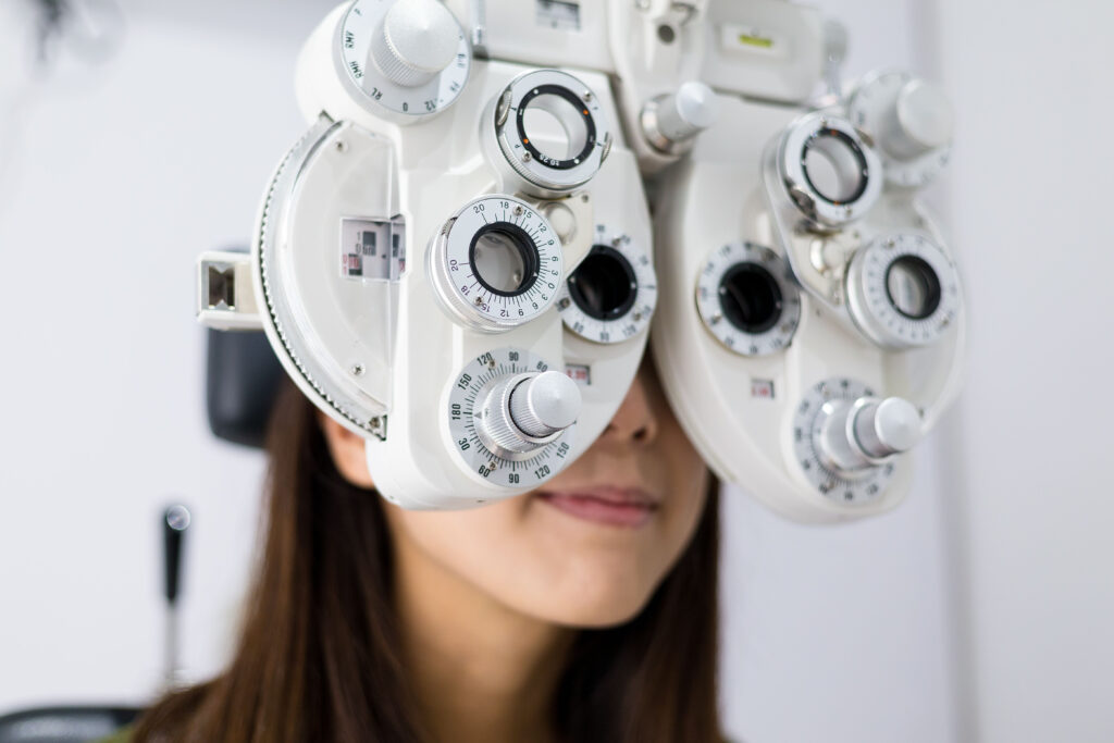 A woman at the eye doctor looking through a phoropter.