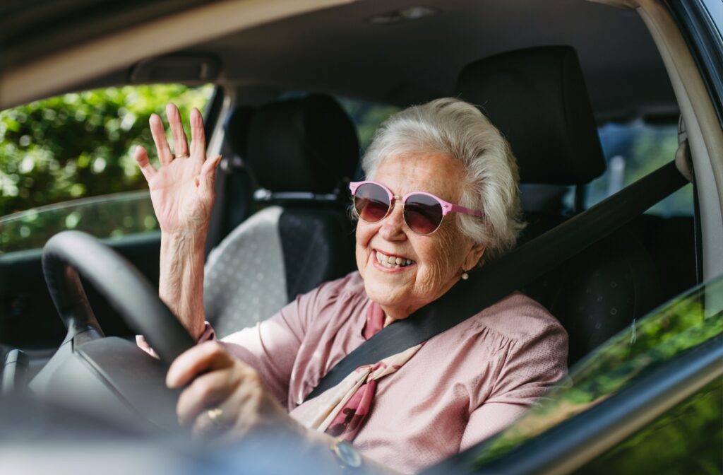 A mature woman in sunglasses, smiles brightly as she drives to her cataract surgery consultation.