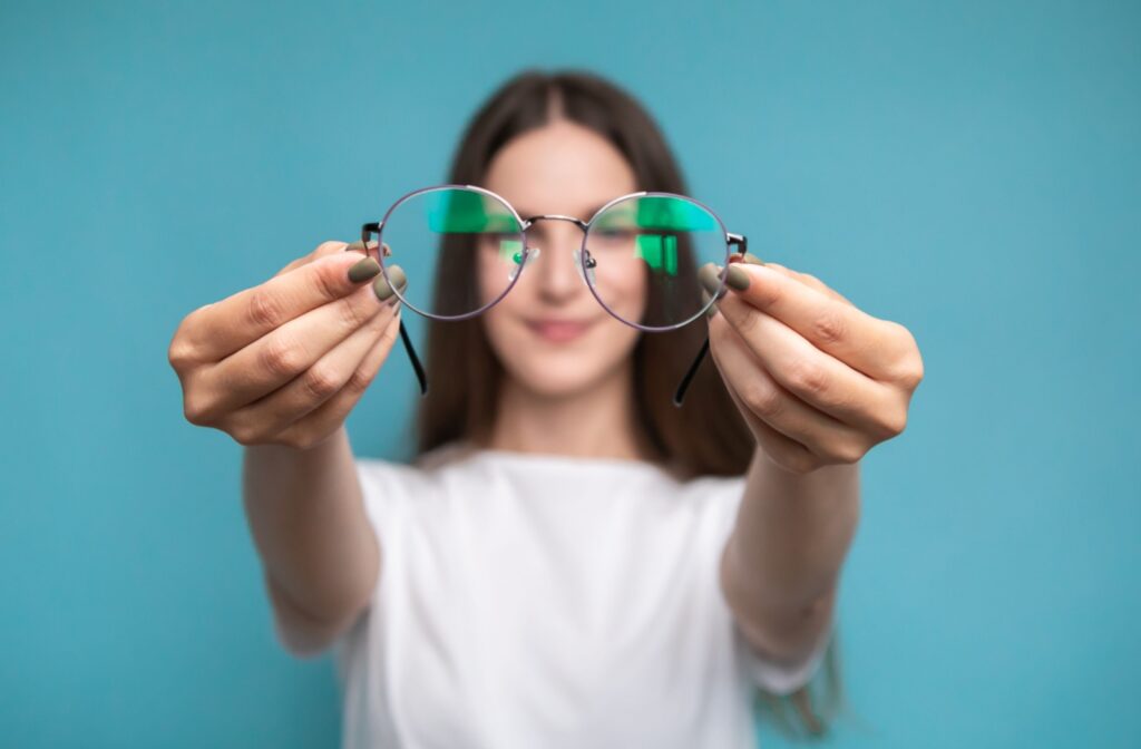 A young patient holding their glasses towards the camera while they stand unfocused in the background.