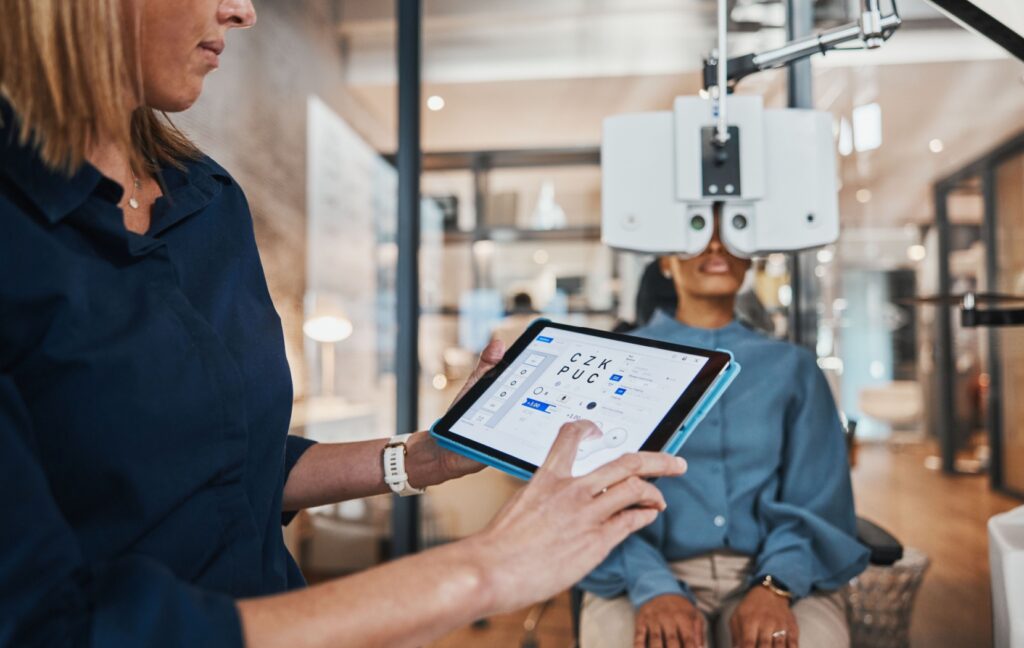 An optometrist uses a tablet to do a visual acuity test on their patient sitting in the optometrist's modern office.