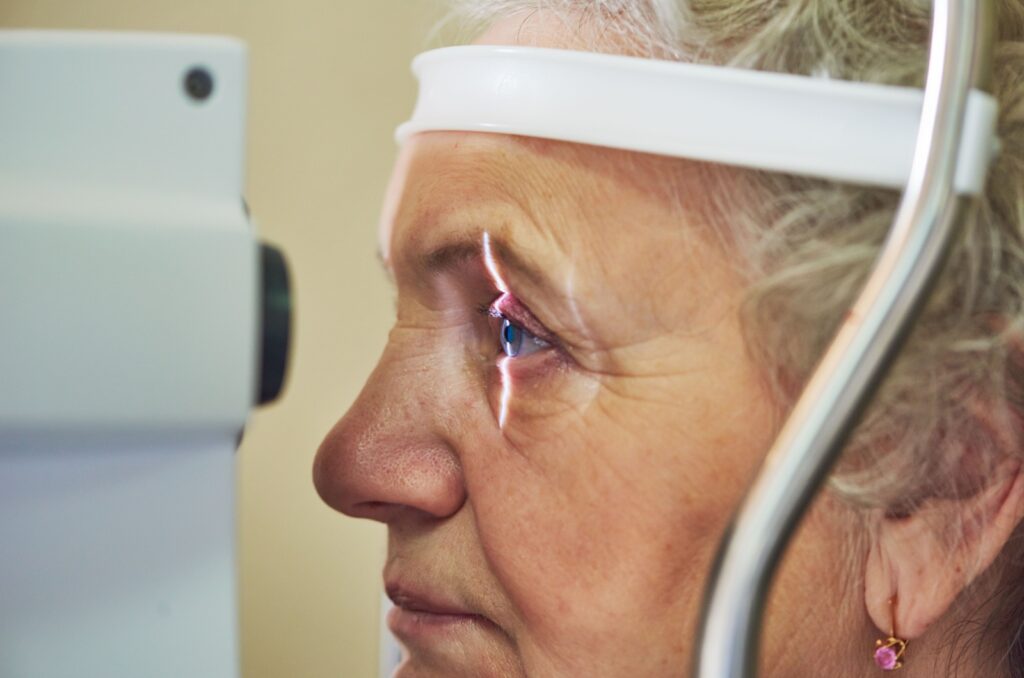 An older adult looking into an optical equipment with light shining in their eyes during an eye exam.