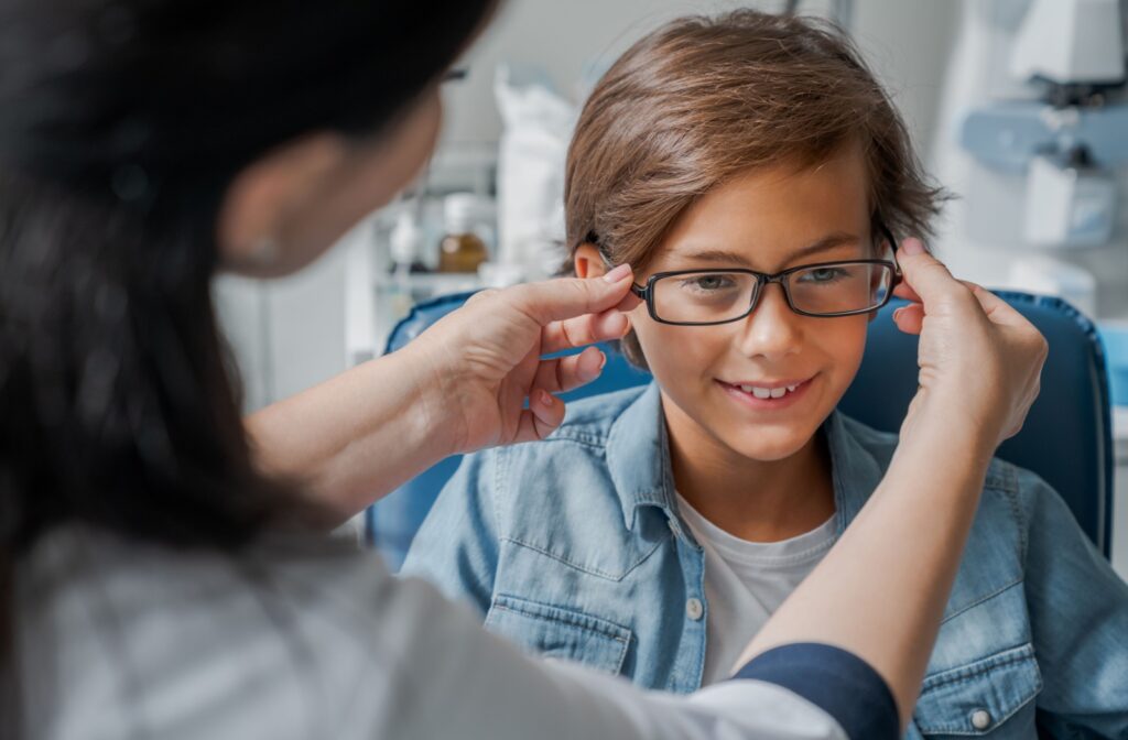 A smiling child having glasses fitted by an optometrist in an office, with the optometrist adjusting the frames for a comfortable fit.