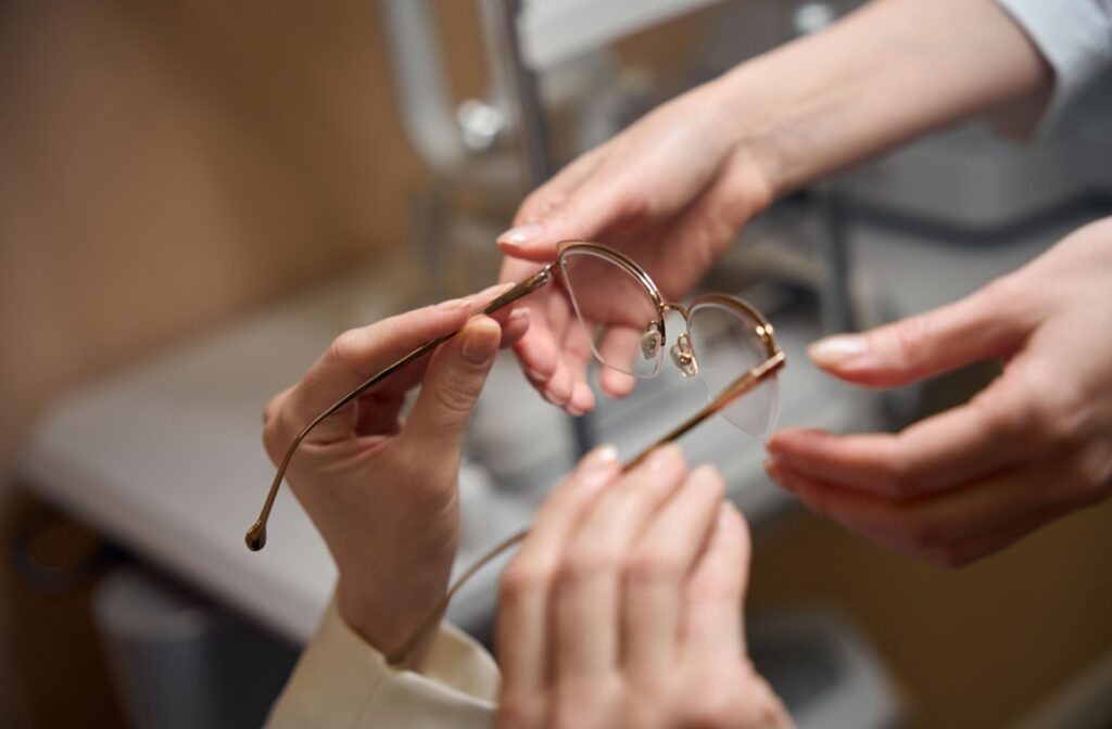 An optometrist handing a pair of glasses to a patient, completing the fitting process in a professional office setting.