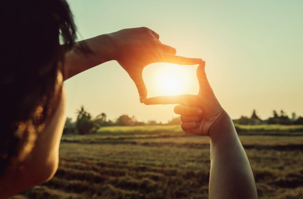 Woman framing sun on the horizon with her fingers.