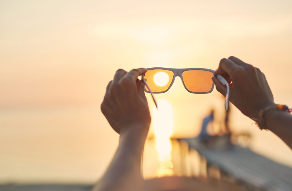 Person holding up sunglasses to the sun at a beach pier.