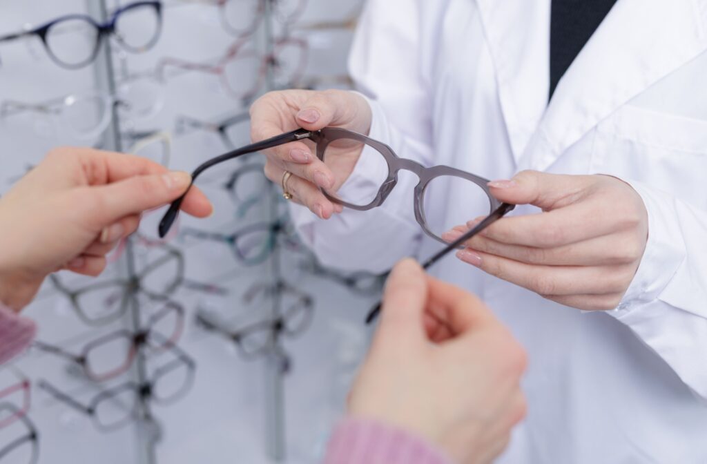 An optician handing a pair of glasses with an updated prescription and lens features to help with digital eye strain to a patient.