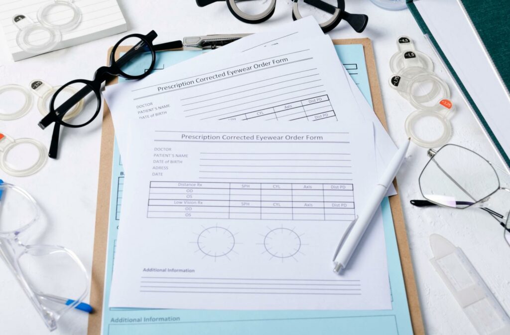 A clip board with an eyeglass prescription form on it, surrounded by different frames and lenses.