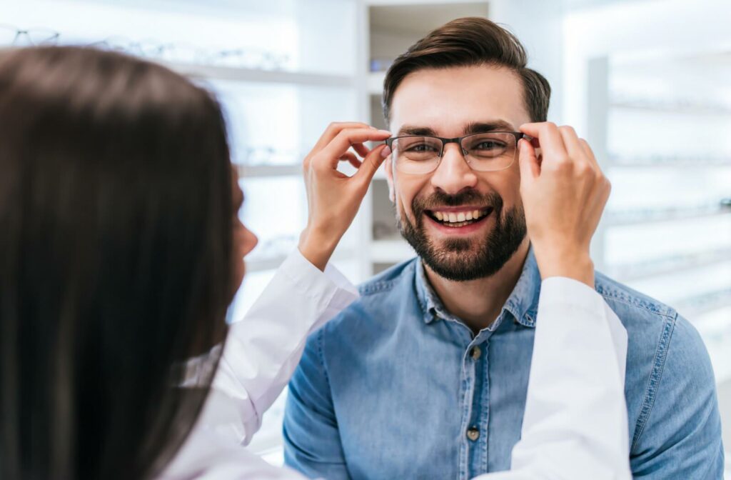 An optician fitting a new pair of eyeglass frames to a patient's face.